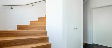 Una escalera con escalones de madera y barandilla de metal, que lleva a una puerta blanca.
