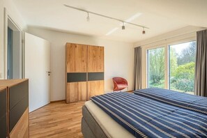 A bedroom with a large bed, a wardrobe, and a window with a view of greenery. - Holiday apartment with 2 bedrooms (Uhldingen-Mühlhofen)