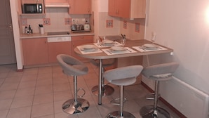 Een kleine keuken met een magnetron, broodrooster en een eethoek met twee barstoelen.