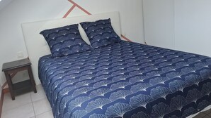 Een bed met een donkerblauwe bedspreide en passende kussens, een klein houten nachtkastje en een wit hoofdbord.