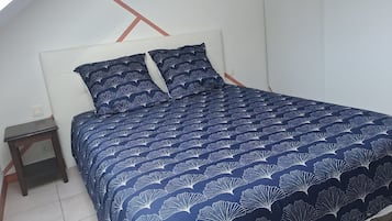 Een bed met een donkerblauwe bedspreide en passende kussens, een klein houten nachtkastje en een wit hoofdbord.