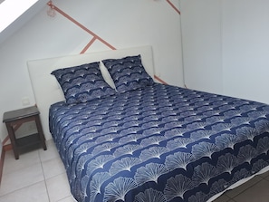 A bed with a dark blue patterned bedspread and matching pillows, a small wooden nightstand, and a white headboard. - Beautiful apartment located right in the heart of Burgundy (Levernois)