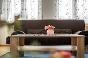 Ein Holztisch mit Blumen in einer Vase vor einer dunkelgrauen Couch.