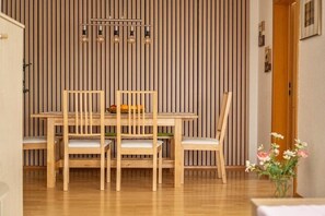 Ein Essbereich mit einem Holztisch und Stühlen, einer Leuchte darüber und einer Wand aus Holz mit vertikalen Linien.