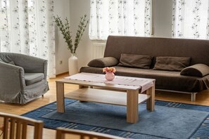 Ein Wohnzimmer mit einer Couch, einem Couchtisch, einem Sessel und einer Vase mit Blumen.