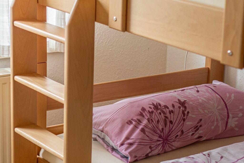 Un lit superposé avec une structure en bois et un seul coussin rose à motifs floraux.