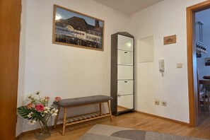 Ein Zimmer mit einer Bank, einem Schrank, einem gerahmten Bild an der Wand und einem kleinen Tisch mit Blumen.