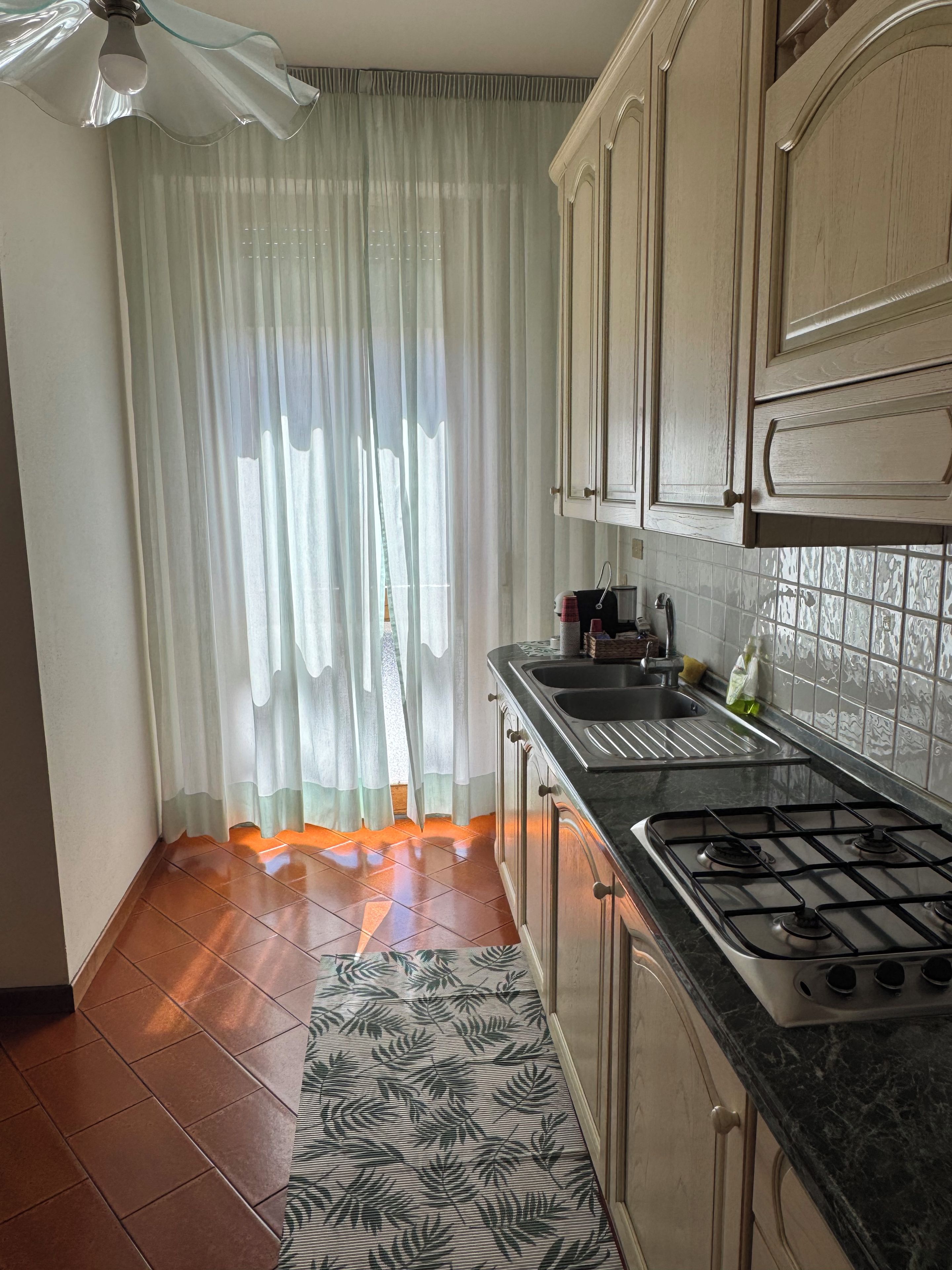 A kitchen with a gas stove, a sink, and a patterned rug.