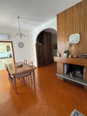 A dining area with a wooden table and chairs, a kitchen in the background, and a wooden wall with a decorative plate. - Marisa's Home (Santa Croce sull'Arno)
