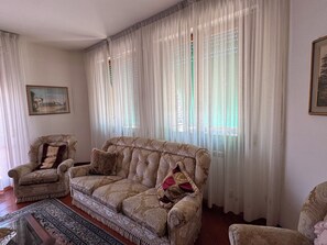 Ein Wohnzimmer mit einem gemusterten Sofa, Sesseln, einem Teppich und einem Gemälde an der Wand.