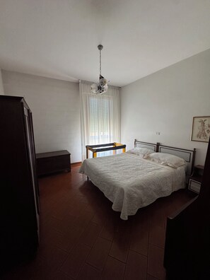 Ein Schlafzimmer mit Bett, einer Bank, einer Hängelampe und einem Fenster mit Vorhängen.