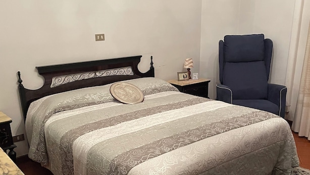 A bedroom with a bed, a nightstand, a chair, a rug, and an air conditioning unit. - Marisa's Home (Santa Croce sull'Arno)
