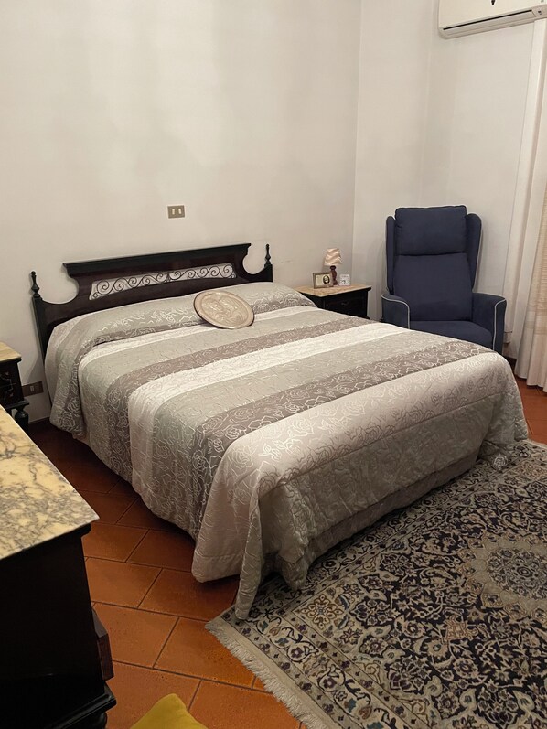 A bedroom with a bed, a nightstand, a chair, a rug, and an air conditioning unit. - Marisa's Home (Santa Croce sull'Arno)