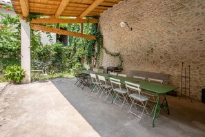 An outdoor patio with a stone wall, a wooden pergola, a table with chairs, and a grill. - Mas Carpe Diem (sleeps 14) with a pool and game room, ideal for families (Orthoux-Sérignac-Quilhan)