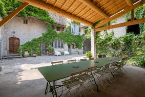 A covered outdoor dining area with a long table and chairs, surrounded by stone walls and greenery. - Vrbo Property (Orthoux-Sérignac-Quilhan)