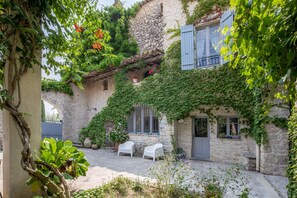 A stone building with ivy-covered walls, a balcony with blue shutters, and two white chairs in the courtyard. - Vrbo Property (Orthoux-Sérignac-Quilhan)