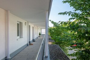 Ein Korridor mit Geländer, Fliesenboden und Blick auf Grünflächen sowie ein geparktes Auto.