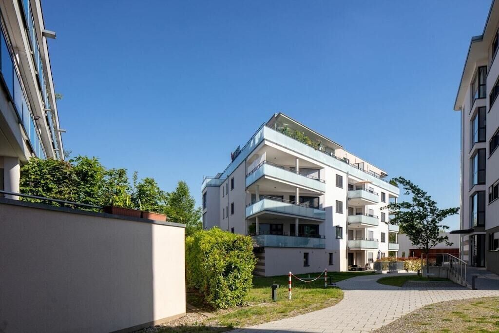 A multi-story residential building with balconies, a paved courtyard, and a clear sky.