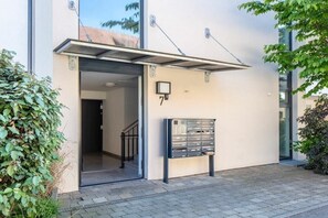 Ein moderner Gebäudeeingang mit Metallvordach, Briefkasten und einer Treppe, die zu einem Innenbereich führt.