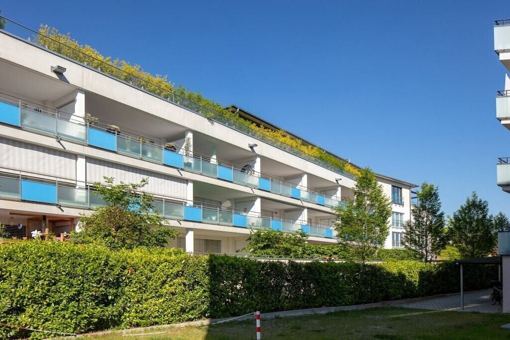 Un edifici residencial de diversos pisos amb balcons, cel blau i vegetació.
