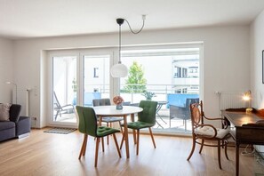 Ein modernes Wohnzimmer mit Essbereich, großen Fenstern und Blick auf ein Gebäude.