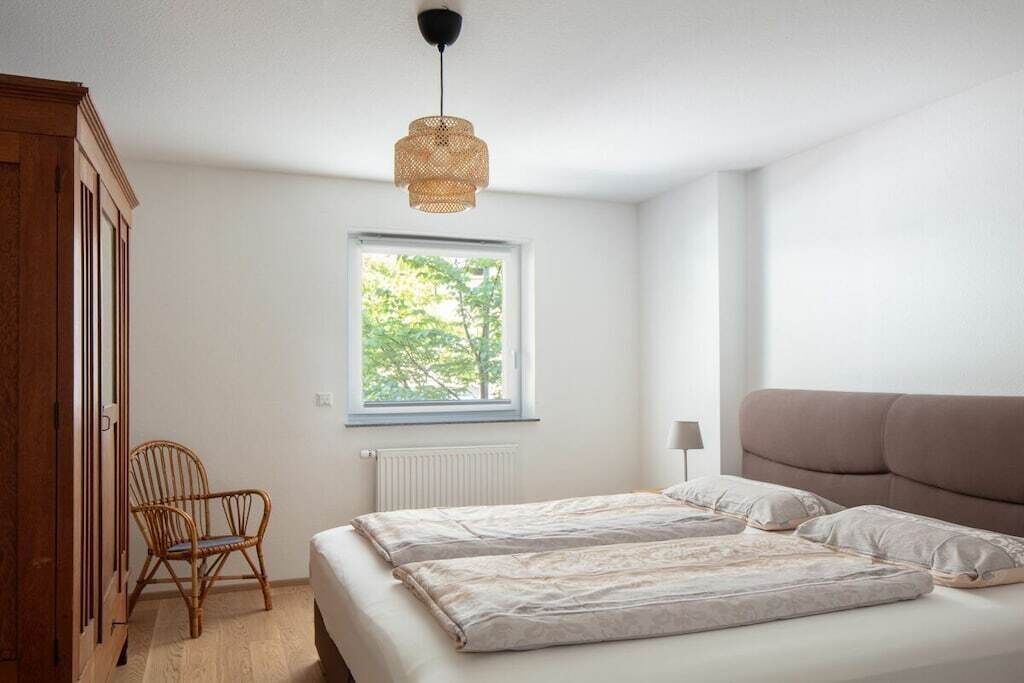 A bedroom with a bed, a window, a chair, and a hanging light fixture.