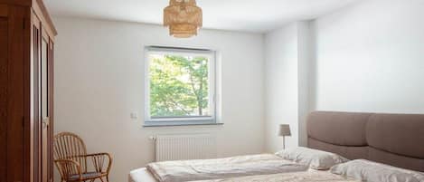 A bedroom with a bed, a window, a chair, and a hanging light fixture.