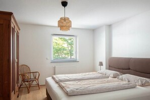 A bedroom with a bed, a window, a chair, and a hanging light fixture. - Holiday apartment with 1 bedroom (Überlingen)