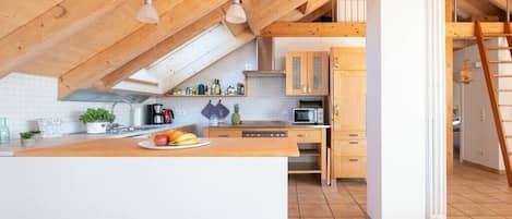 A kitchen with a wooden ceiling, a central island, and a view of a lofted sleeping area.