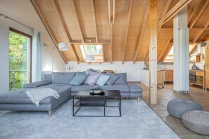 A modern loft-style living space with a high ceiling, a sectional sofa, a coffee table, and a view of the kitchen. - Holiday apartment with 1 bedroom (Überlingen)