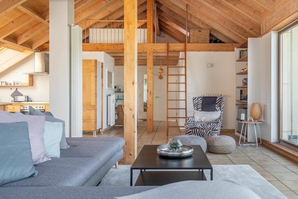 A spacious living area with a high ceiling, a sofa, a coffee table, a zebra-patterned chair, and a bookshelf.