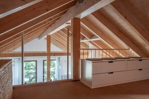 Habitación en ático con vigas de madera a la vista, un banco blanco empotrado y vistas a la vegetación.