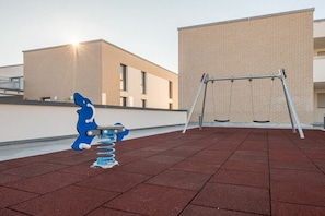 Ein Spielplatz mit Schaukeln und einer blauen Kletterkonstruktion auf einer roten, gummiartigen Oberfläche.
