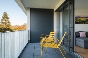 Ein Balkon mit zwei gelben Stühlen, einem grauen Sofa und einer Glastür zu einem Zimmer.