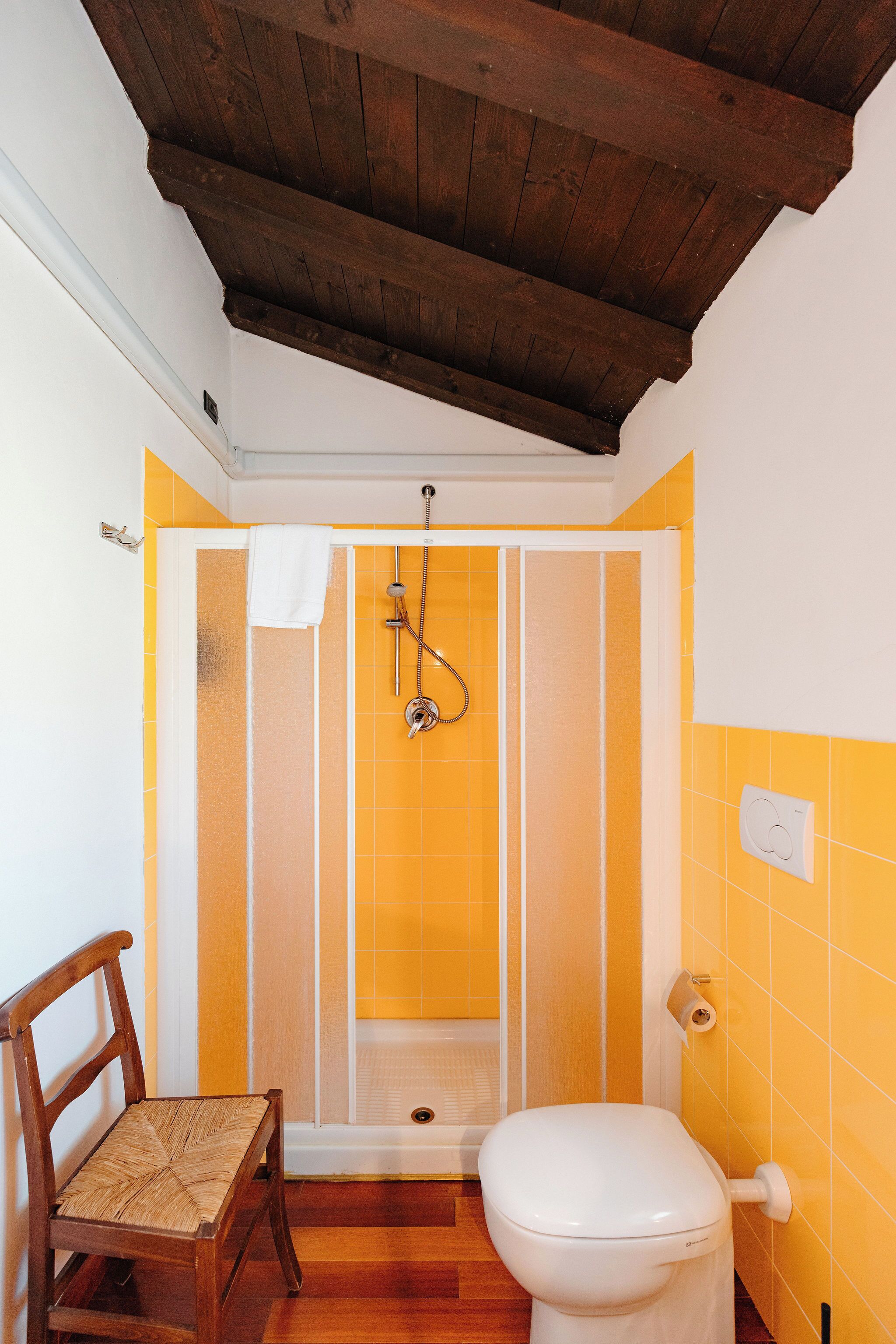 A bathroom with a shower, toilet, and a wooden chair.