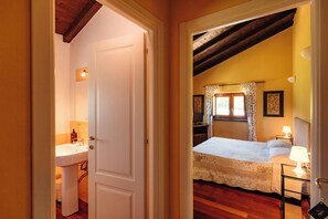 A bedroom with a bed, a nightstand, a lamp, a window with curtains, and a door leading to a bathroom. - Tenuta Bellingeri - Locanda del Barco (SANT AGATA FOSSILI)