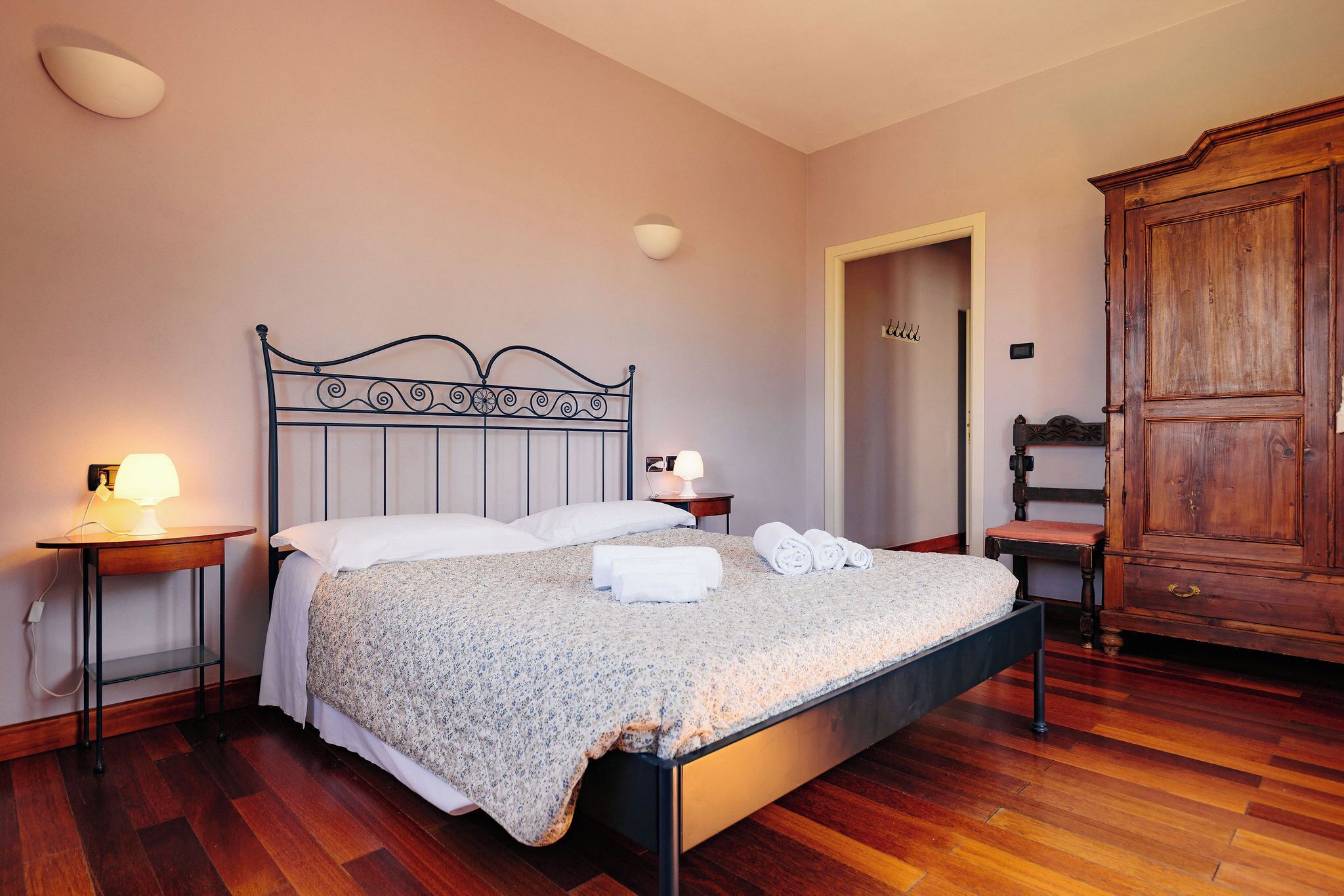 Una cama bien tendida con una colcha floral, dos lámparas de noche, un armario de madera y un piso de madera.
