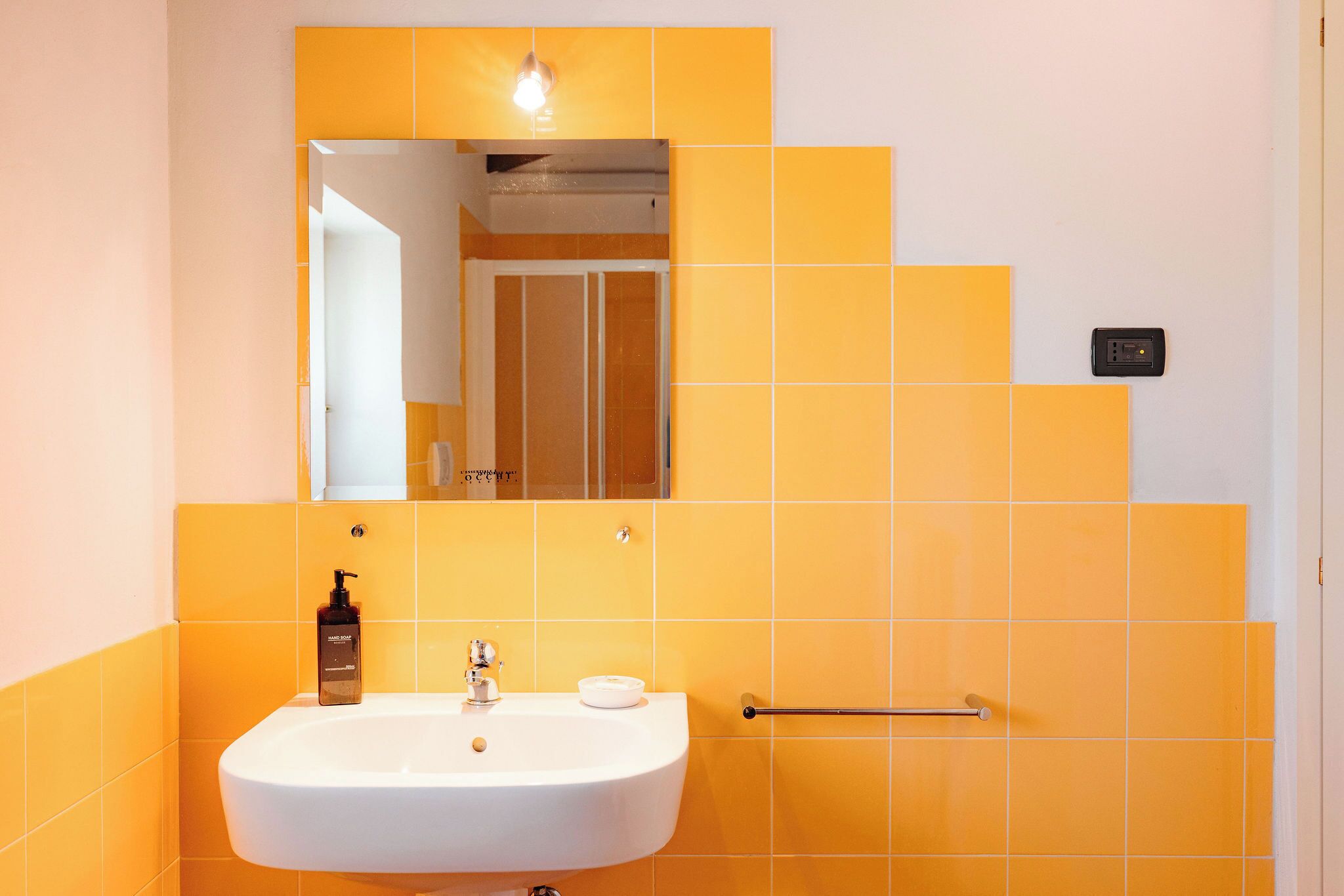 Un baño con lavamanos blanco, un espejo y azulejos amarillos.