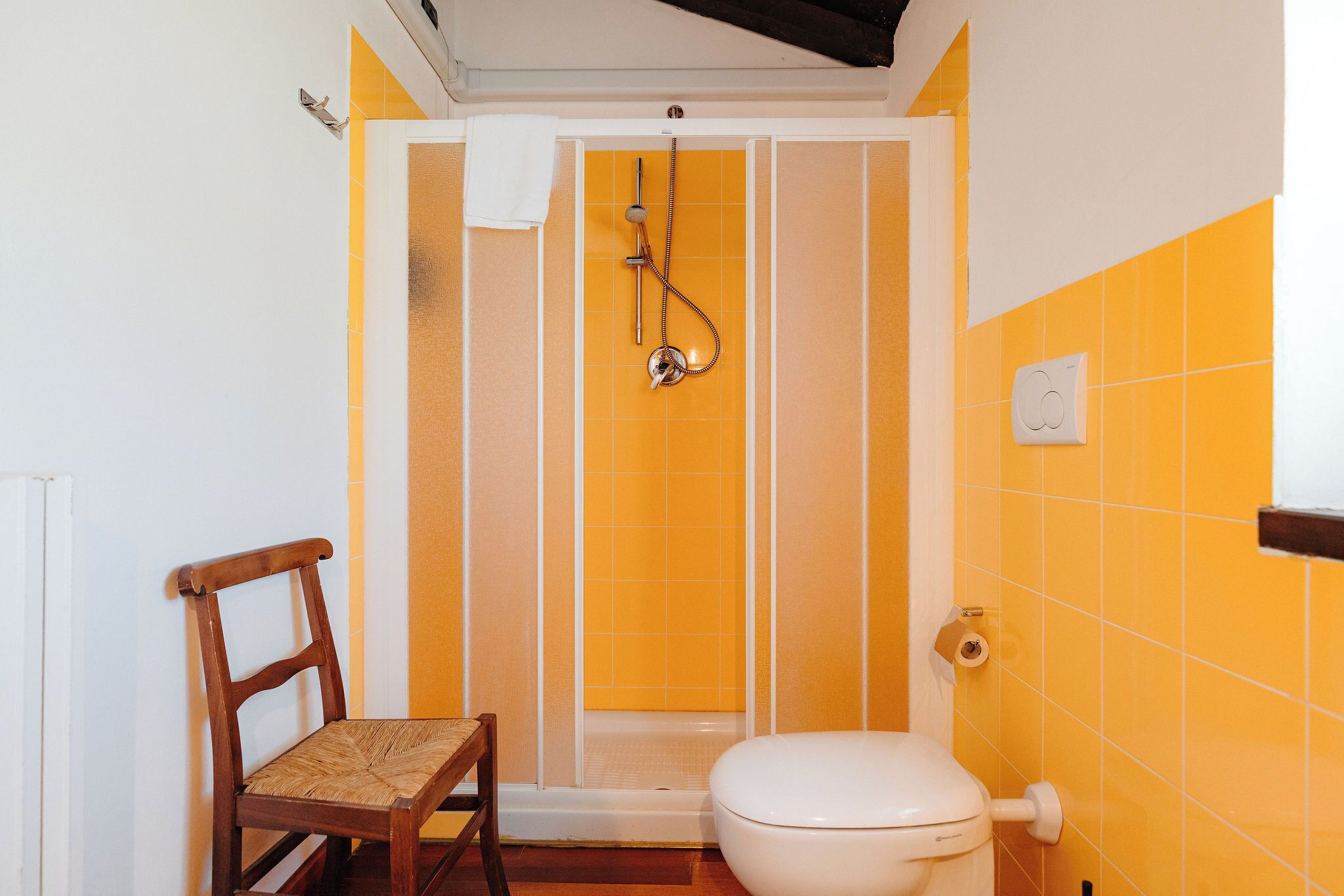 Un baño con ducha, inodoro y una silla de madera.