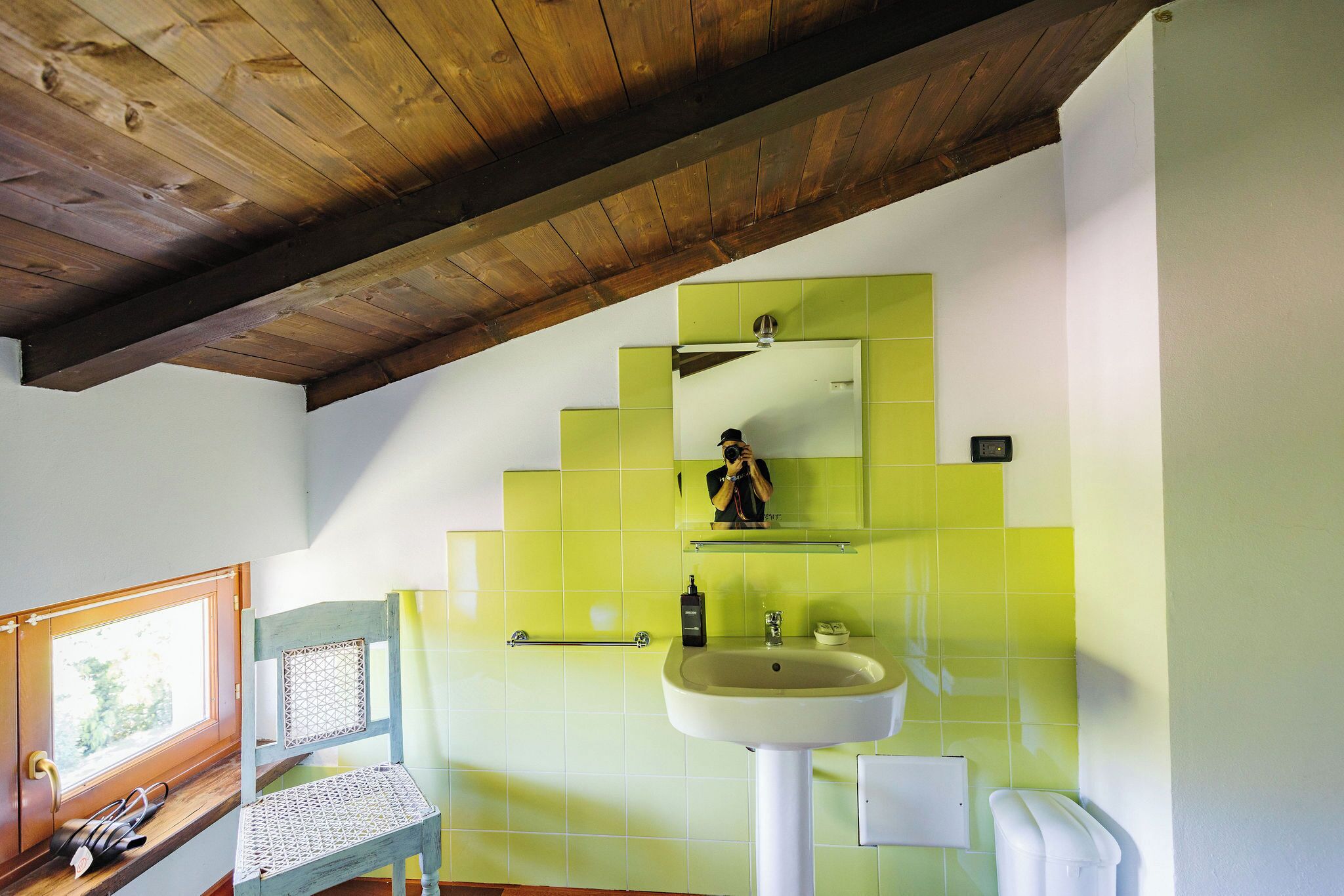 A bathroom with a wooden ceiling, a sink, a mirror, and a window.
