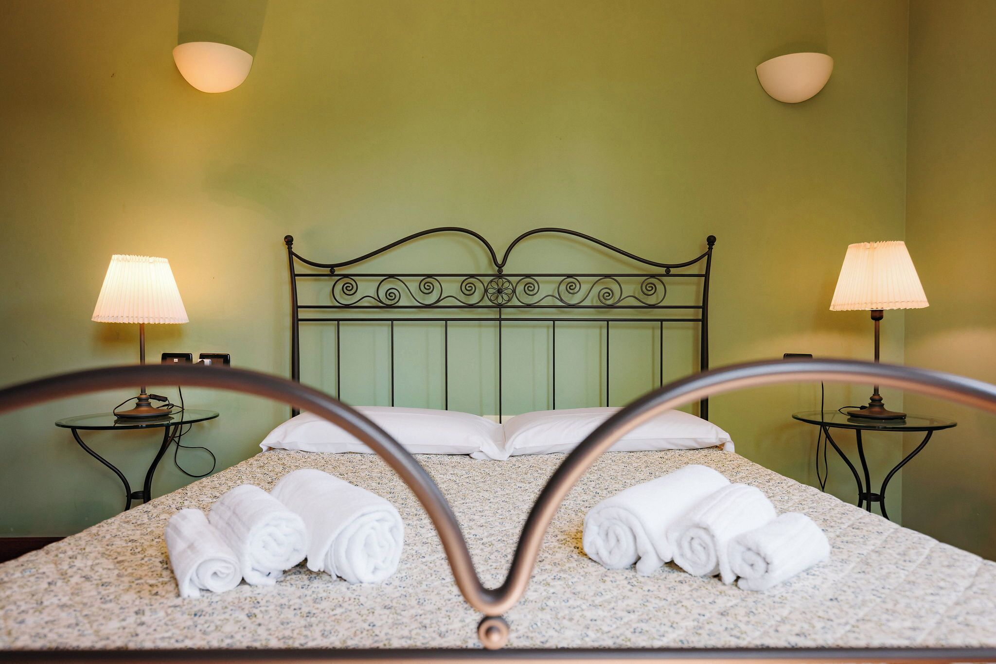 Una habitación de hotel con una cama, dos lámparas de noche y toallas enrolladas.