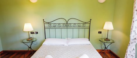 Una cama bien tendida con dos almohadas, dos mesitas de noche con lámparas, y una pared verde.