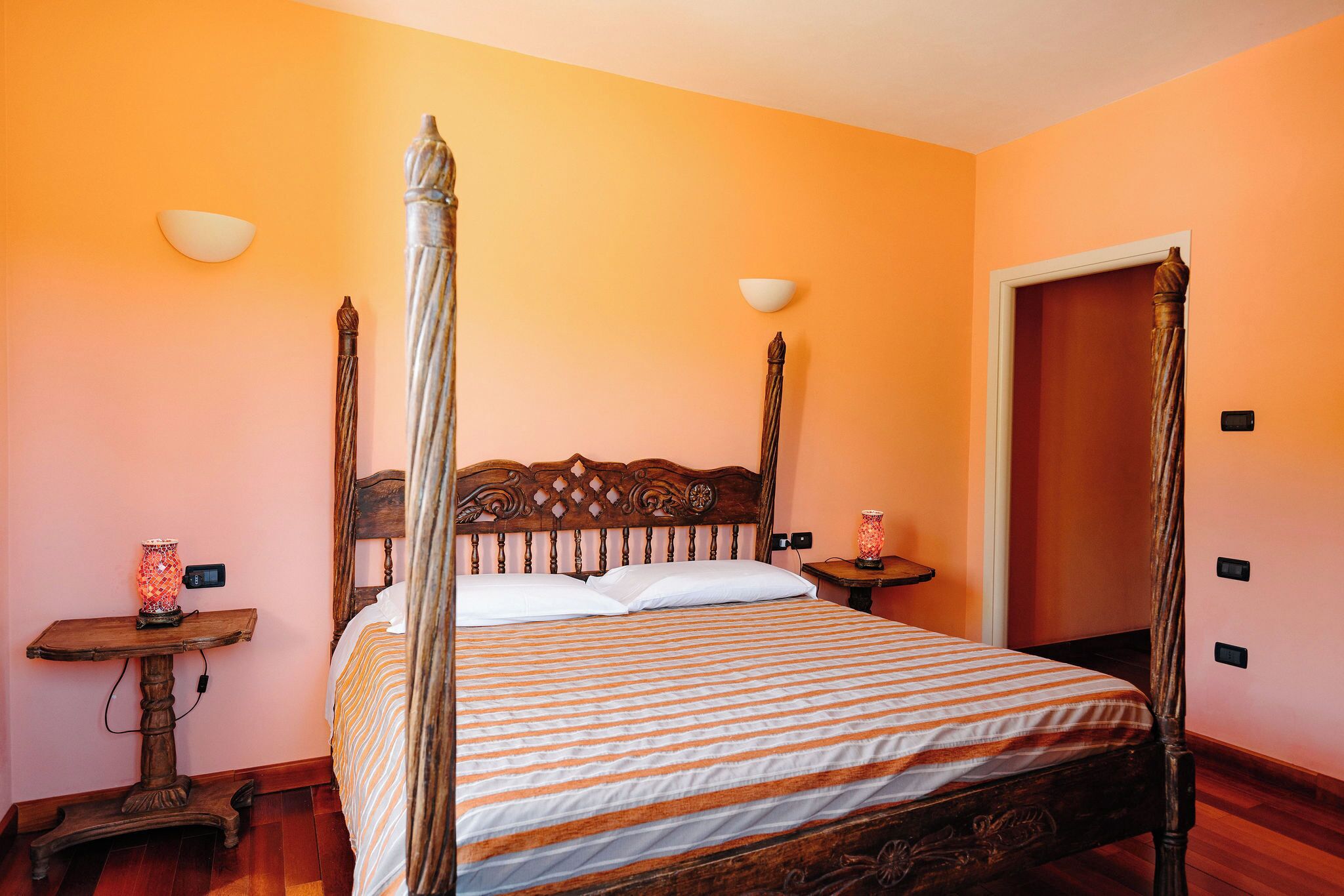 Un letto a baldacchino con copripiumino a righe, un comodino con una lampada e un lampadario a parete.