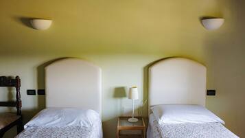Two single beds with white linens, a wooden nightstand with a lamp, and a chair.