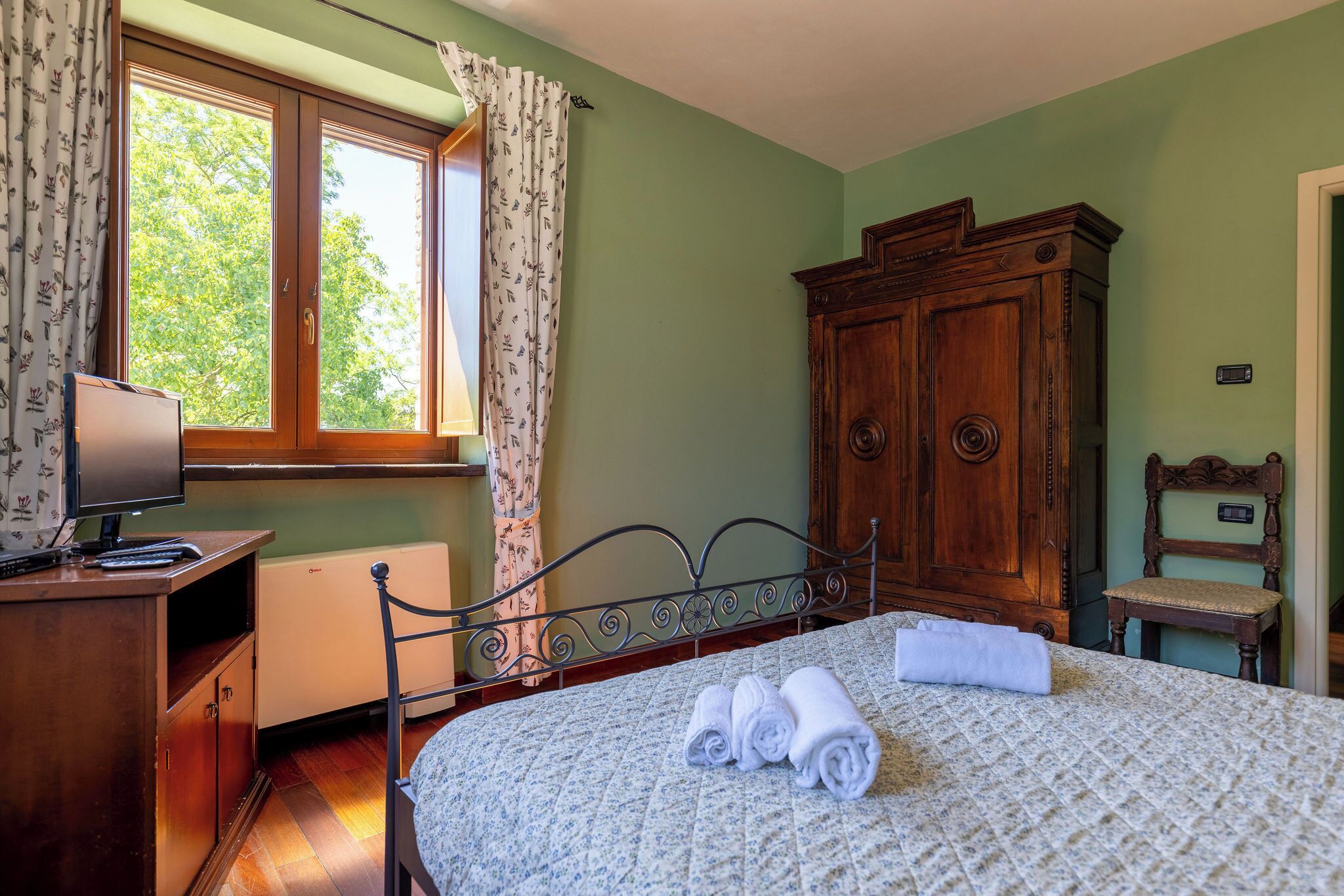A bedroom with a bed, a desk, a chair, a wardrobe, and a window with curtains.