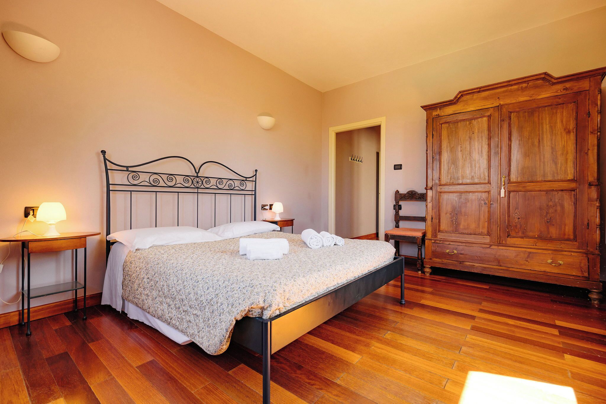 A bedroom with a bed, bedside tables, a wardrobe, and a door leading to another room.