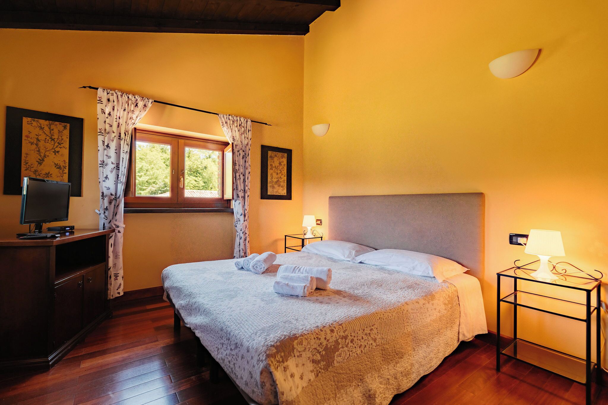 Een hotelkamer met een bed, een bureau met een computer, een raam met gordijnen en een bedlamp.