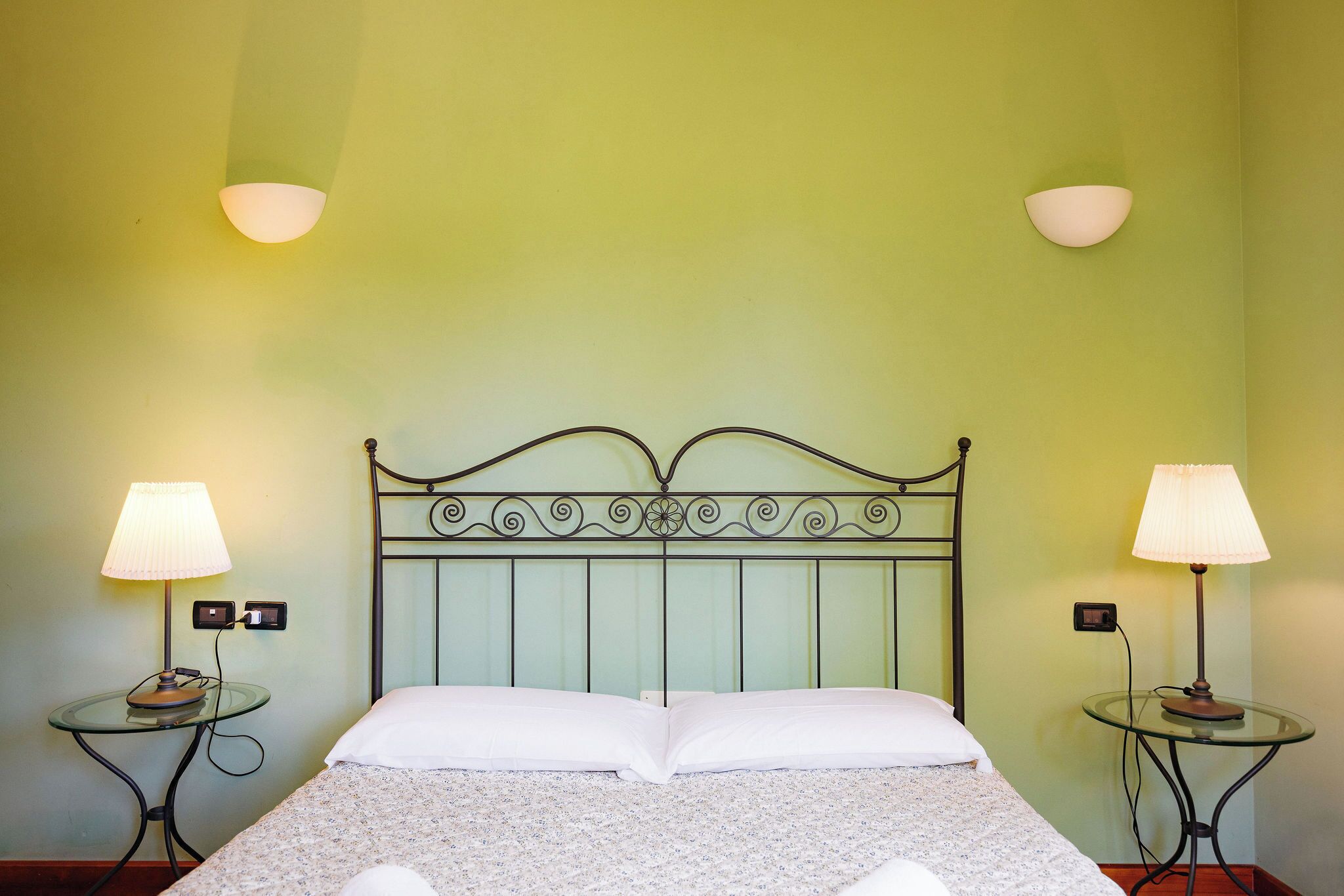 A bed with a metal headboard, two bedside lamps, and a wall-mounted switch.