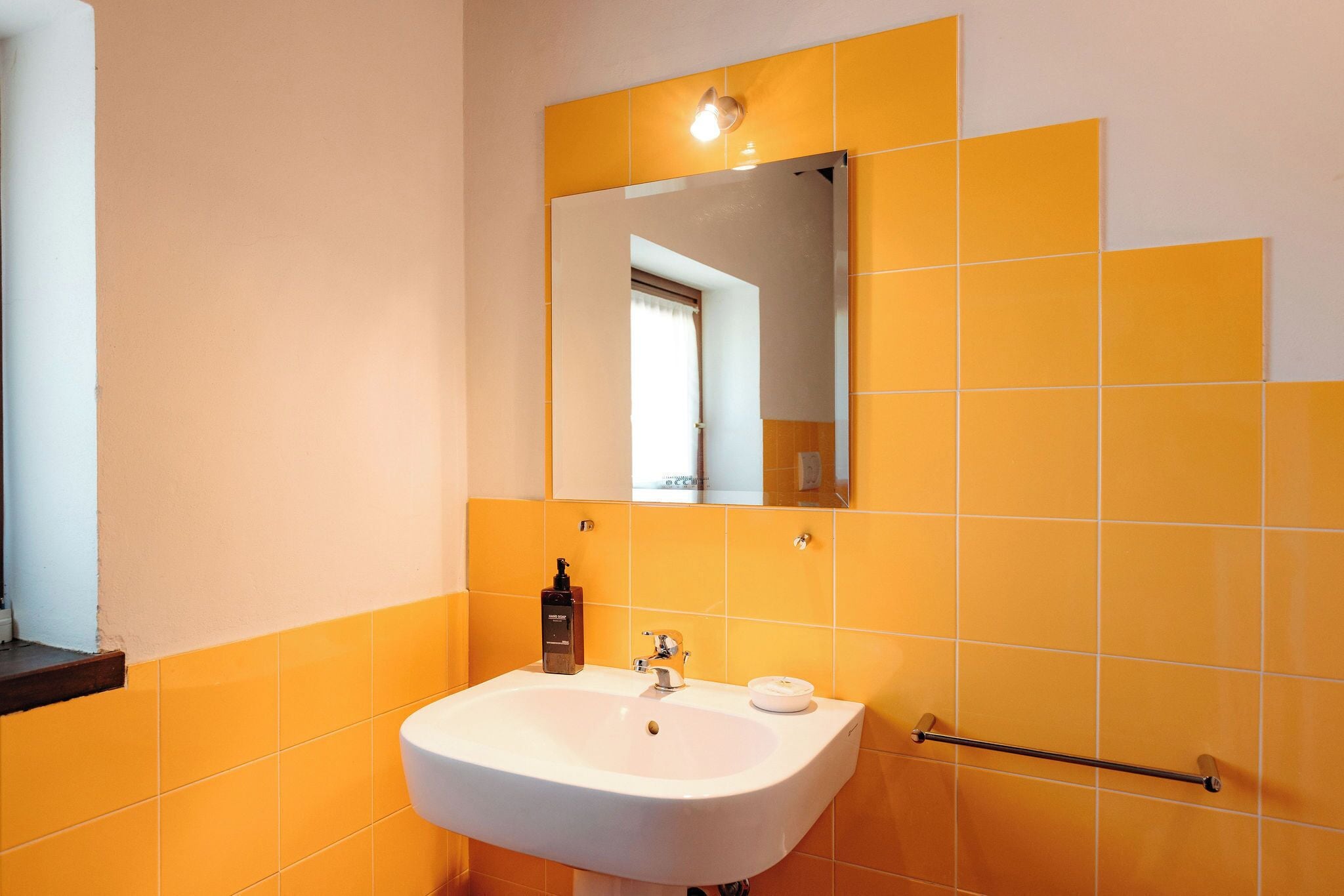 Un baño con lavamanos blanco, un espejo y azulejos anaranjados.