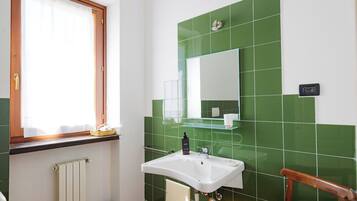 Een badkamer met een wit wastafel, groene tegels, een houten stoel en een raam met houten kader.